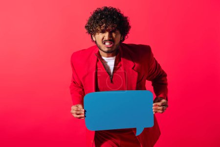Photo for A vibrant young man in a red suit holds a blue speech bubble against a vivid backdrop. - Royalty Free Image
