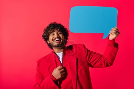 A stylish Indian man in red jacket holding a blue speech bubble against a vivid backdrop.
