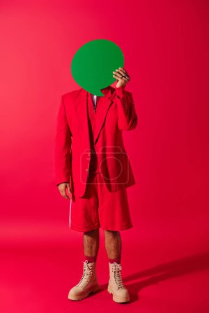 Foto de Hombre indio guapo en traje rojo sostiene burbuja de habla verde por encima de la cabeza en el fondo vívido. - Imagen libre de derechos