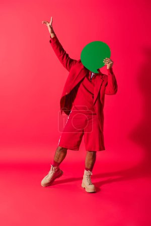 Foto de Guapo joven indio con un vibrante traje rojo sosteniendo juguetonamente una burbuja de habla verde. - Imagen libre de derechos