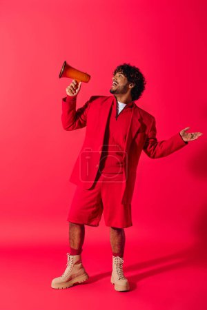 Young Indian man in vibrant red suit holds a red megaphone against a vivid backdrop.