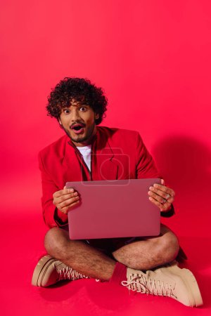 Foto de Un hombre en traje vibrante se sienta en el suelo, absorto en su computadora portátil. - Imagen libre de derechos