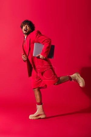 Photo for A handsome young Indian man in a vibrant red suit working on a laptop. - Royalty Free Image