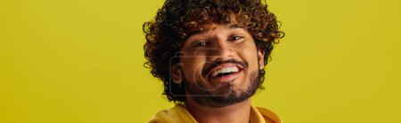 Foto de Un guapo joven indio con el pelo rizado posando en una vibrante camisa amarilla. - Imagen libre de derechos