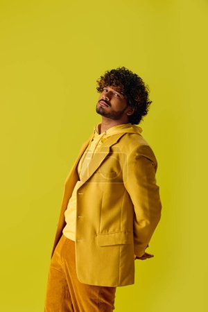 Guapo joven indio en traje vibrante posa delante de una pared de color amarillo brillante.