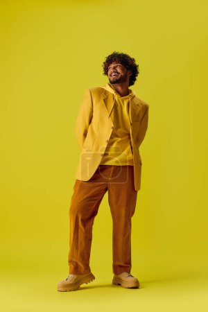 A handsome young Indian man in a vibrant yellow suit stands against a matching yellow background.