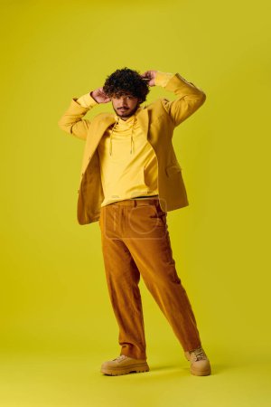Handsome Indian man in vibrant outfit posing on yellow backdrop.