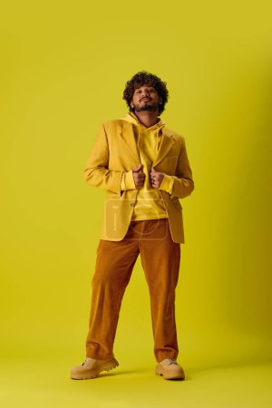 Handsome young Indian man poses in vibrant outfit against vivid yellow backdrop.