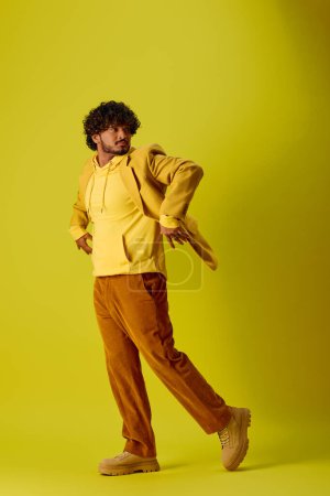 Foto de Hombre indio guapo en camisa amarilla y pantalones marrones posando sobre fondo colorido. - Imagen libre de derechos