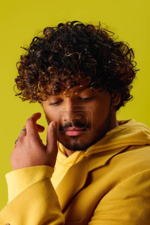 Foto de Hombre indio guapo con el pelo rizado en una sudadera con capucha amarilla llamativa, posando sobre un telón de fondo vívido. - Imagen libre de derechos