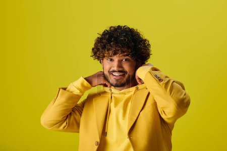 Handsome young Indian man in a yellow jacket smiling on a vibrant backdrop.