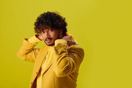 Handsome young Indian man in a yellow jacket holding his hands to his ears.