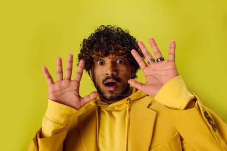 Foto de Hombre indio guapo en chaqueta amarilla vibrante que se divierte posando con las manos en la cara. - Imagen libre de derechos
