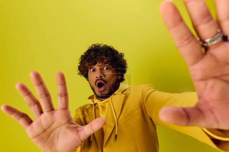 A handsome young Indian man in a yellow hoodie is making a gesture.