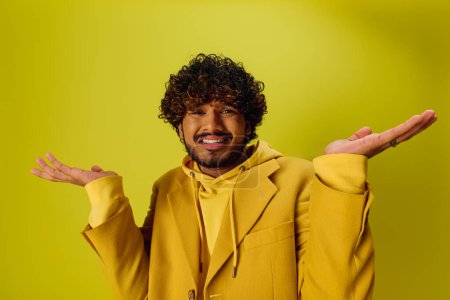 Schöner indischer Mann mit lockigem Haar in auffälliger Pose in leuchtend gelber Jacke.