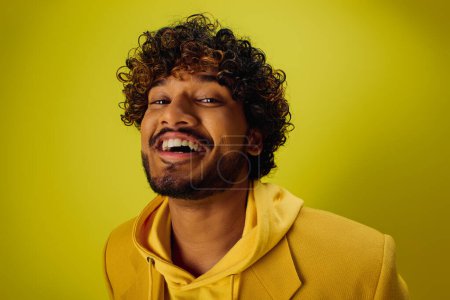 Handsome Indian man with curly hair poses confidently in a bright yellow hoodie.