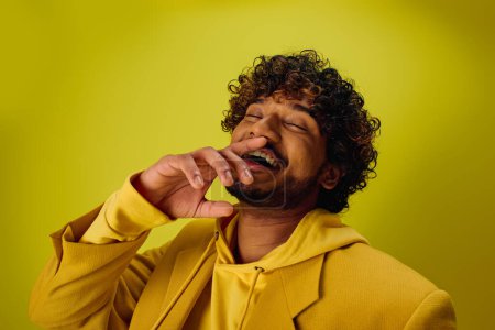 Ein gutaussehender, junger indischer Mann in einem gelben Kapuzenpullover vor einer lebhaften Kulisse.
