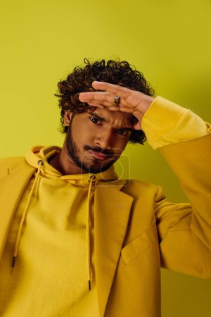 Handsome young Indian man with curly hair posing in a vibrant yellow hoodie.