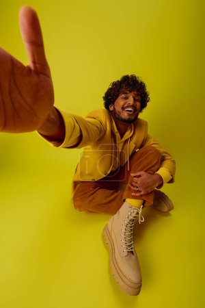 Photo for Handsome young Indian man in vibrant outfit sitting on the ground with foot up. - Royalty Free Image
