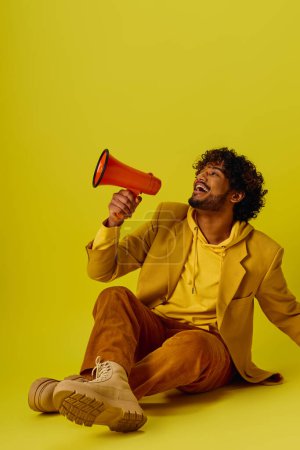 Photo for A stylish Indian man sits holding a red and black megaphone. - Royalty Free Image