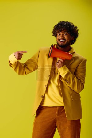 Hombre indio guapo en chaqueta amarilla sosteniendo megáfono rojo contra fondo vívido.
