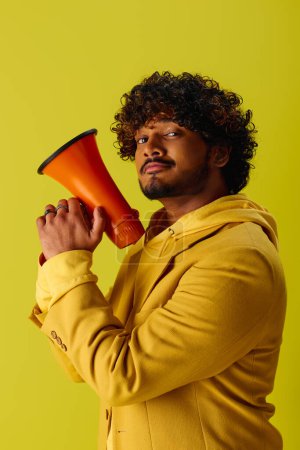 A handsome young Indian man in a vibrant outfit holding a red and black megaphone.