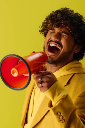 Hombre joven indio guapo en traje amarillo llamativo llama la atención con megáfono rojo y negro.