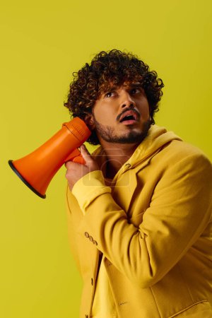 Handsome young Indian man in yellow jacket holding red and orange megaphone.