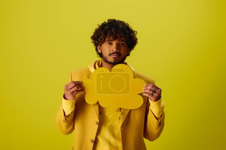 Handsome young Indian man in a yellow suit holding a speech bubble.
