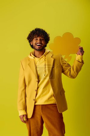 Handsome young Indian man in vibrant yellow jacket and brown pants posing against vivid backdrop.
