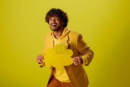 Handsome Indian man in vibrant yellow jacket holding a delicate speech bubble.