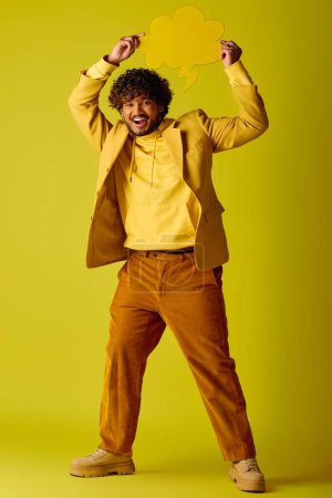 Foto de Hombre indio guapo en camisa amarilla y pantalones marrones, posando frente a un fondo vívido. - Imagen libre de derechos