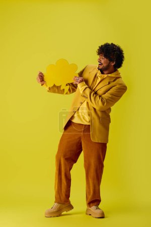 Young Indian man in yellow jacket holds a yellow speech bubble against vibrant backdrop.