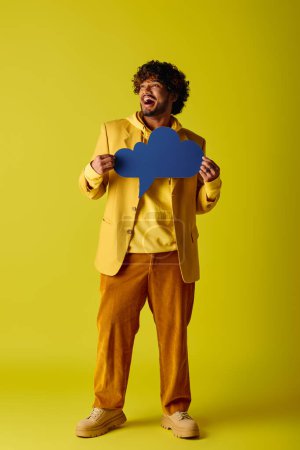 Handsome Indian man in vivid yellow suit holds a vibrant blue speech bubble.