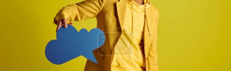 Photo for Handsome young Indian man in yellow raincoat holding a blue speech bubble against a vivid backdrop. - Royalty Free Image