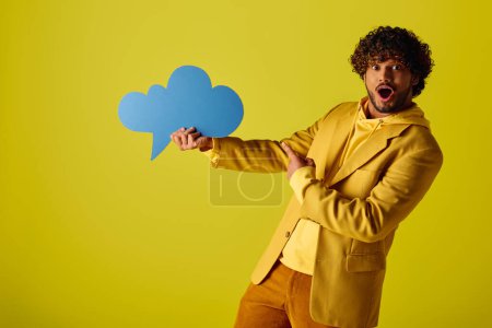 Young Indian man stylishly holds a speech bubble in a vibrant yellow jacket against a colorful backdrop.