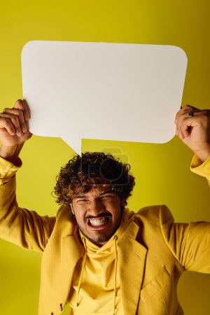 A handsome young Indian man in a yellow suit holds a white speech bubble.