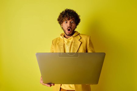 Ein stilvoller junger Inder im gelben Anzug, selbstbewusst in der Hand einen Laptop.