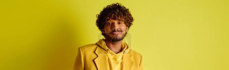 Handsome young Indian man in vibrant outfit standing confidently in front of a bright yellow wall.