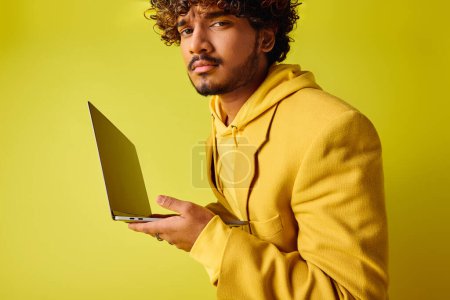 Ein hübscher junger indischer Mann in lebendiger Kleidung hält einen Laptop in der Hand.