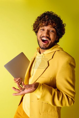 Photo for Handsome Indian man in a vibrant yellow suit confidently holds a laptop. - Royalty Free Image