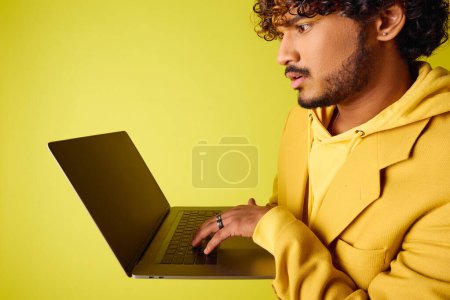 Handsome young Indian man with curly hair using a laptop on a vibrant backdrop.