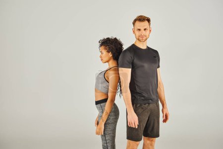 Photo for Young interracial sport couple confidently stands in front of a gray background, exuding strength and unity. - Royalty Free Image