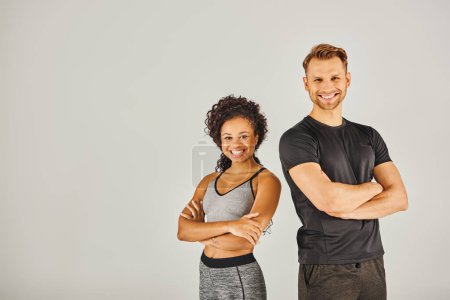 Un jeune couple sportif interracial, vêtu de vêtements actifs, posant ensemble dans un studio sur un fond gris.