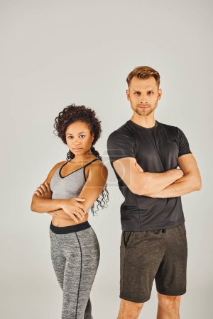 Ein junges interrassisches Sportpaar in aktiver Kleidung posiert gemeinsam vor grauem Hintergrund in einem Studio-Setting.