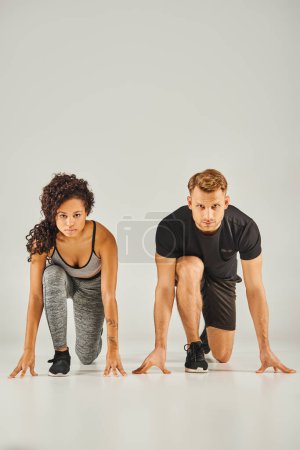 A young interracial sport couple wearing active wear demonstrating perfect squat form in unison on a white background.