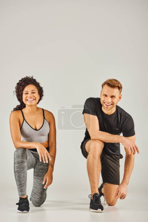 Foto de Joven pareja deportiva interracial en cuclillas juntos en ropa activa sobre fondo gris en un entorno de estudio. - Imagen libre de derechos