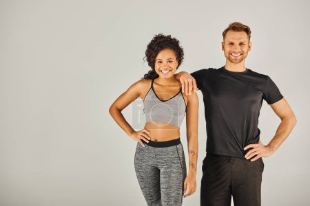 Foto de Un hombre joven y una mujer en ropa deportiva hacen una pose de moda juntos contra un fondo gris del estudio. - Imagen libre de derechos