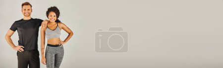 Téléchargez les photos : Un jeune couple sportif interracial en tenue active élégante posant en toute confiance devant un fond gris neutre. - en image libre de droit