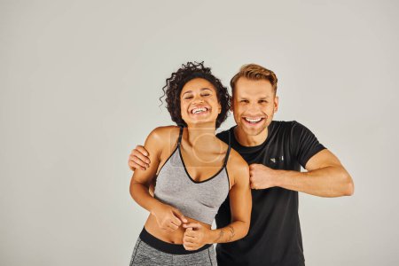 Una joven pareja deportiva interracial en ropa activa posando con confianza para la cámara en un estudio sobre un fondo gris.